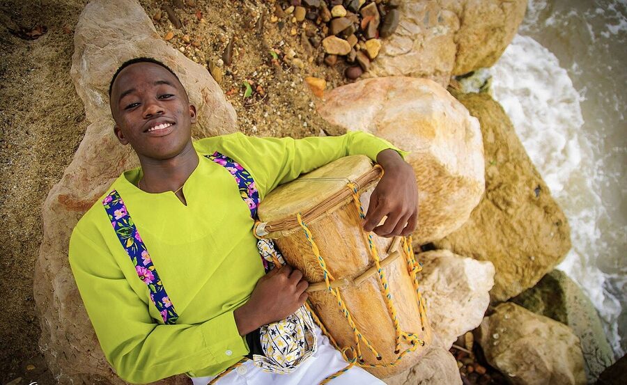 Young Garifuna drummer in traditional clothes holding a drum by the sea in Dangriga, Belize