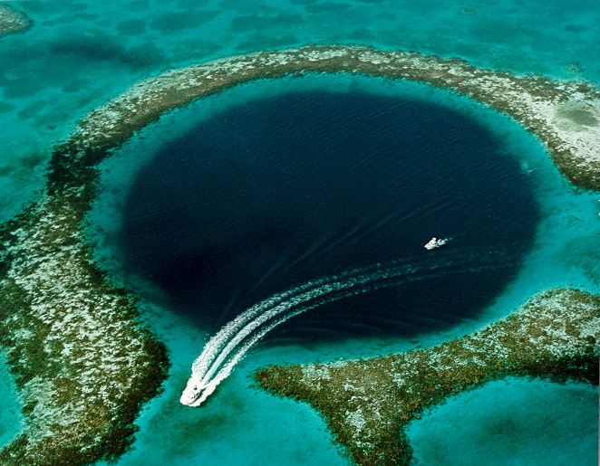 Aerial view of the Great Blue Hole in Belize, a perfect dark circle in turquoise water with a small boat