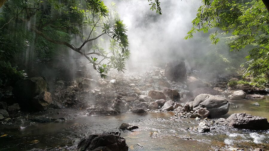 Steamy hot springs in Honduras with mist rising from rocks in a forested gorge