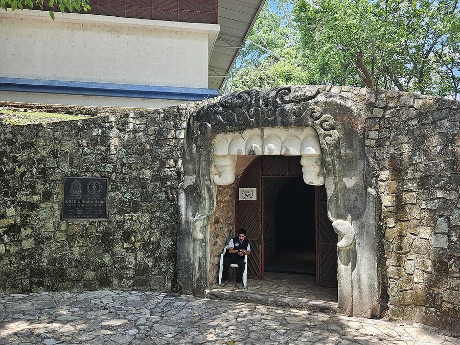 Original Mayan stone carving displayed inside the Copán Sculpture Museum, showing a god mask with curling features and inset eyes