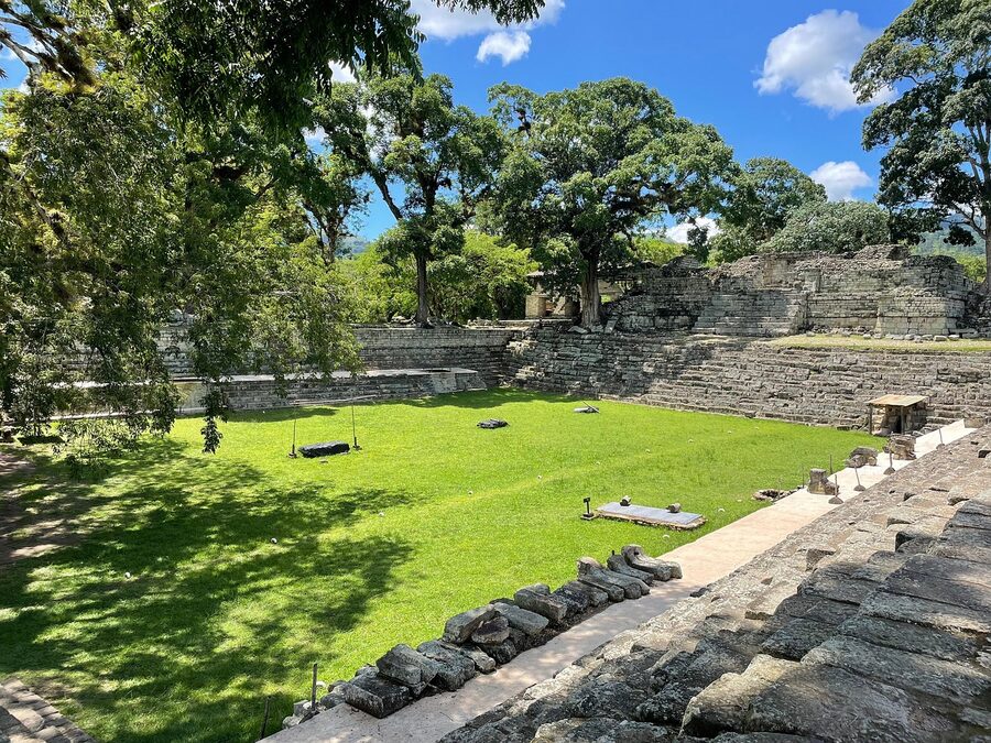 Gran Plaza of the Copán archaeological site, Honduras, looking out across the cleared central area at low stone platforms and shaded trees