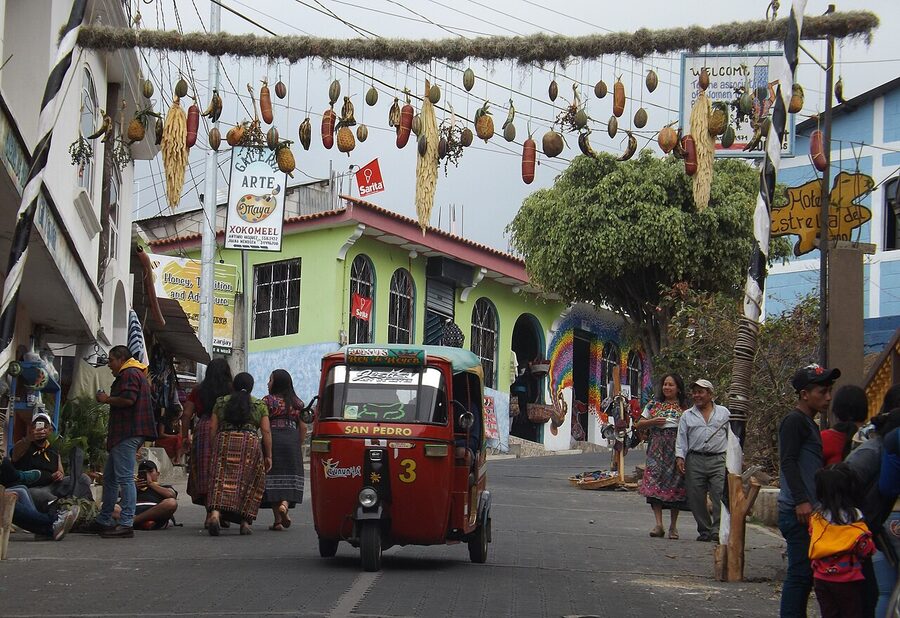 Main street of San Juan La Laguna with hanging coffee and corn decorations and a red tuk-tuk to San Pedro