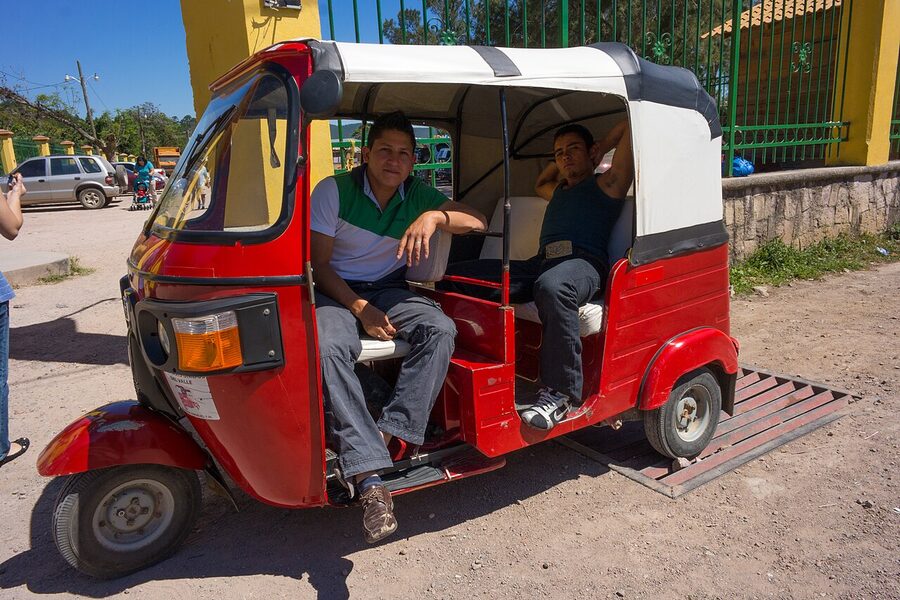 Red and white mototaxi rickshaw with two men sitting inside in Valle de Angeles